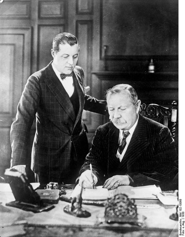Der berühmte englische Schriftsteller Conan Doyle der berühmte Veter der bekannten Cherlock-Holmes-Romane ist, 71 Jahre alt, in London gestorben. Unser Bild zeigt den berühmten englischen Schriftsteller Conan Doyle bei der Arbeit an seinem Schreibtisch. Stehend sein Sohn Adrian Doyle.