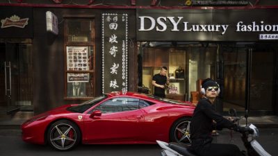 Китаец пользуется телефоном рядом со своим Ferrari в престижном торговом районе Пекина 29 мая 2015 г. (Кевин Фрайер / Getty Images)