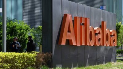 Двое сотрудников Alibaba беседуют за вывеской Alibaba возле офиса компании в Пекине, 13 апреля 2021 года.. Фото: GREG BAKER/AFP via Getty Images