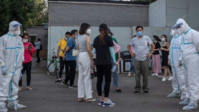 Сотрудники, одетые в средства индивидуальной защиты, возле группы людей в масках, ожидающих  тестирования на COVID-19 в Пекине 19 июня 2020 года. NICOLAS ASFOURI/AFP via Getty Images