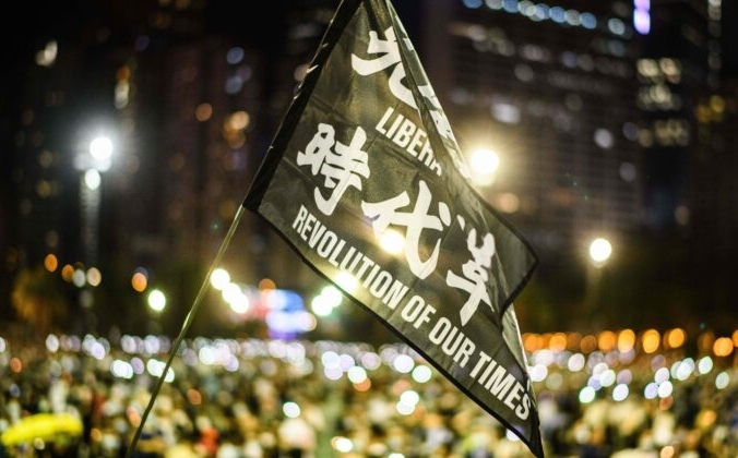 Участники митинга поднимают флаг с надписью «Освободите Гонконг, революция нашего времени» во время акции при свечах в парке Виктория в Гонконге 4 июня 2020 года. ANTHONY WALLACE/AFP via Getty Images