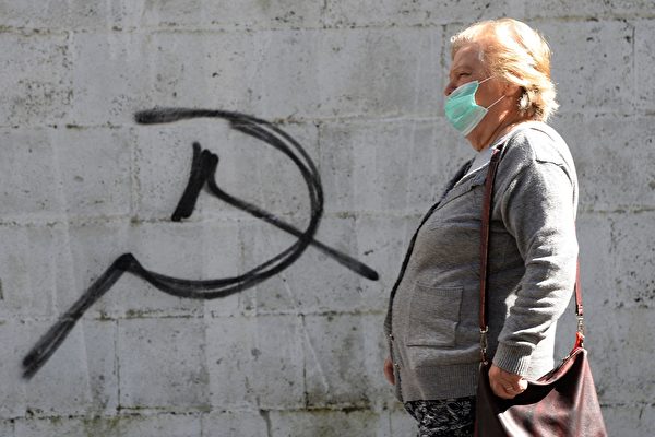 Женщина в маске проходит мимо символа серпа и молота во время ярмарки в городе Карбальино, на северо-западе Испании, 16 мая 2020 года