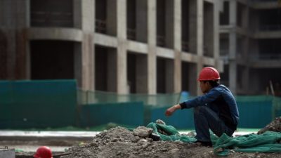 Строитель отдыхает возле здания в новом финансовом районе города Тяньцзинь на севере Китая, 14 мая 2015 года. Один масштабный правительственный проект включает десятки небоскребов. Он рассматривается как будущий «китайский Манхэттен». Но замедление темпов роста экономики увеличило сомнения в жизнеспособности таких проектов, учитывая увеличение числа «городов-призраков» в стране. Фото: Greg Baker/AFP/Getty Images