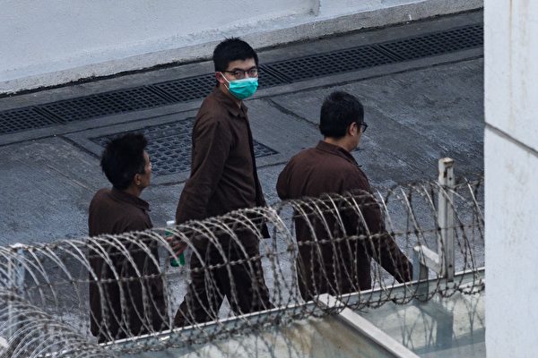 Активист Джошуа Вонг (в центре) идёт по территории приемного центра Лай Чи Кок в Гонконге 3 декабря 2020 года после того, как его заключили в тюрьму за участие в прошлогоднем митинге у здания полиции