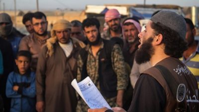 На этом фото от 14 мая 2015 года на сайте боевиков, сотрудник «полиции нравов» ИГИЛ*, известной как «Хисба», читает приговор, вынесенный судом ИГИЛ*, в котором нескольких людей признают виновными в прелюбодеянии, город Ракка, Сирия. Фото: theepochtimes.com
