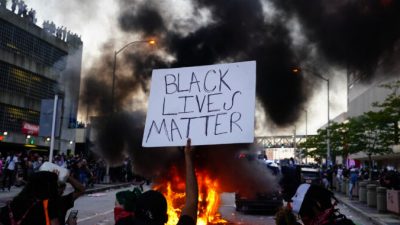 Мужчина держит знак Black Lives Matter, когда горит полицейская машина во время акции протеста в Атланте, Джорджия, 29 мая 2020 года. Elijah Nouvelage/Getty Images