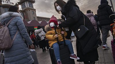 Мать везёт чемодан, на котором сидит девочка в защитной маске, чтобы сесть на поезд на железнодорожном вокзале Пекина перед ежегодным праздником весны, Пекин, Китай 21 января 2020 года. Kevin Frayer/Getty Images