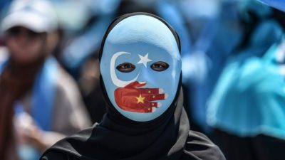 Демонстрант в маске, раскрашенной в цвета флага Синьцзяна, принимает участие в акции протеста, осуждающей обращение Китая с этническими мусульманами-уйгурами, перед китайским консульством в Стамбуле 5 июля 2018 года. (OZAN KOSE/AFP/Getty Images)