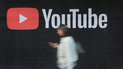 Женщина со смартфоном проходит мимо рекламного щита YouTube в Берлине 27 сентября 2019 г. (Sean Gallup/Getty Images)