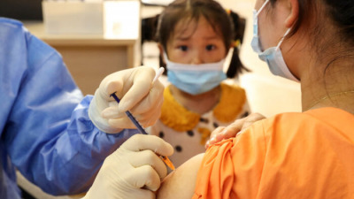 Ребёнок наблюдает, как женщина получает вакцину COVID-19 Китайской национальной биотехнологической группы (CNBG) в Наньтуне, в восточной провинции Китая Цзянсу, 5 июля 2021 г. (STR / AFP через Getty Images)