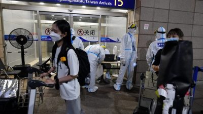 Работники аэропорта Пудун в защитной одежде помогают прибывающим пассажирам сесть в автобусы, которые отвезут их в карантинные отели в Шанхае 13 августа 2021 года. (Greg Baker/AFP)