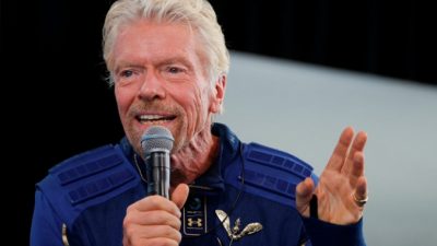 Предприниматель-миллиардер Ричард Брэнсон со значком крильев астронавта на пресс-конференции после полёта с экипажем на пассажирском ракетоплане VSS Unity компании Virgin Galactic к краю космоса в космодроме «Америка» неподалёку от города Truth or Consequences, штат Нью-Мексико, 11 июля 2021 года (Джо Скиппер). / Reuters)