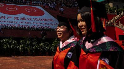 Два выпускника проходят мимо большого плаката к столетию компартии Китая в Уханьском университете в Ухане, Китай, 23 июня 2021 г.
