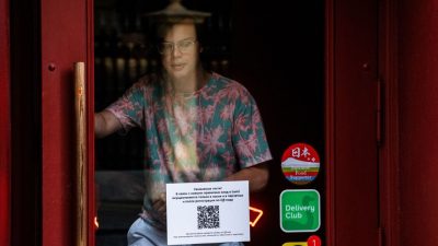 Мужчина выходит из ресторана с табличкой на двери, указывающей на то, что гости должны сначала зарегистрироваться в ресторане с помощью QR-кода, прежде чем смогут занять место. Москва, 22 июня 2021 года. DIMITAR DILKOFF/AFP via Getty Images