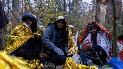 Сирийские мигранты сидят под  одеялами, защищаясь от дождя в лесу недалеко от Хайнувки в Польше, во время совместной спасательной операции активистов Grupa Granica и волонтёров из Medycy na Granicy, 23 октября 2021 года. Тысячи мигрантов, в основном с Ближнего Востока, пересекли или пытались пересечь границу из Беларуси с лета. ЕС считает, что белорусский режим намеренно отправляет мигрантов в ответ на санкции ЕС. WOJTEK RADWANSKI/AFP via Getty Images 