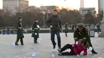 Полицейский толкнул женщину, протестующую против несправедливости в отношении её дела. Женщина бросила листовки, когда её окружила полиция возле столба с государственным флагом на площади Тяньаньмэнь в Пекине 5 марта 2014 г. Alexander F. Yuan/AP Photo