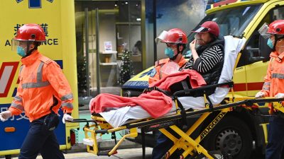 Спасатели несут пострадавшего в машину скорой помощи после пожара во Всемирном торговом центре в Гонконге, 15 декабря 2021 года. (Sung Pi-lung/The Epoch Times)