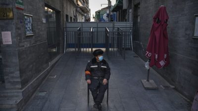 Китайский охранник в защитной маске наблюдает за зоной возле баррикады, отделяющей жилой квартал от коммерческого района в Пекине, Китай, 11 марта 2020 г. (Kevin Frayer/Getty Images) 