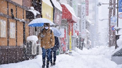 Люди идут по улице в городе Тояма в сильный снегопад, принесённый экстремальным холодным фронтом в западные и северные районы страны 27 декабря 2021 года. (JIJI Press/AFP via Getty Images)
