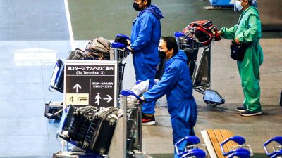 Мужчины в защитных костюмах пробираются к автобусной остановке в международном аэропорту Нарита в первый день закрытых границ в Нарите, к востоку от Токио, Япония, 30 ноября 2021 года. (Kim Kyung-Hoon/Reuters)