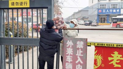 Житель получает еду у входа в жилую зону, закрытую и ограниченную из-за вспышки КОВИД-19 в Аньяне, провинция Хэнань, 12 января 2022 года. (STR/AFP via Getty Images)