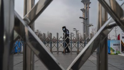 Охранник за шлагбаумом возле Национального стадиона, известного как «Птичье гнездо», который станет частью «пузыря», закрытого для посетителей и местных жителей, на зимних Олимпийских и Паралимпийских играх 2022 года в Пекине. Башня в Олимпийском парке в Пекине, Китай, 19 января 2022 года. (Kevin Frayer/Getty Images) 