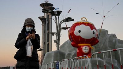 Женщина проверяет свой телефон перед инсталляцией Шуи Рон Рон, талисмана зимних Паралимпийских игр 2022 года в Олимпийском парке в Пекине 13 января 2022 года. Фото: Jade Gao/AFP / Getty Images