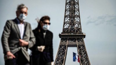 Мужчина и женщина в масках идут по площади Трокадеро на фоне национального флага Франции на Эйфелевой башне в Париже 11 мая 2020 года. Фото: Philippe Lopez/AFP via Getty Images
