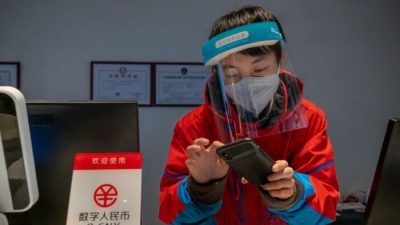  Сотрудник на стойке регистрации отеля Prince Ski Town проверяет телефон за табличкой с надписью «цифровые юани (e-CNY) принимаются» в Чжанцзякоу, Китай, 4 декабря 2021 г. (Andrea Verdelli/Getty Images)