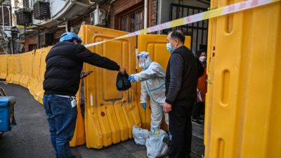 Рабочий в защитном снаряжении охраняет вход в закрытый район в качестве меры против коронавируса Covid-19 и получает еду от курьера в районе Цзинъань в Шанхае, 29 марта 2022 года. Фото: HectorRetamal/AFP viaGettyImages
