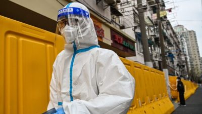 Рабочий в защитном снаряжении идёт рядом с барьерами, отделяющими от улицы квартал, закрытый для посещения в районе Цзинъань, Шанхай, 30 марта 2022 года.