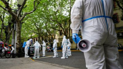 Рабочие в защитных костюмах стоят на улице во время перекрытия движения в Шанхае 16 апреля 2022 года. (Aly Song/Reuters)
