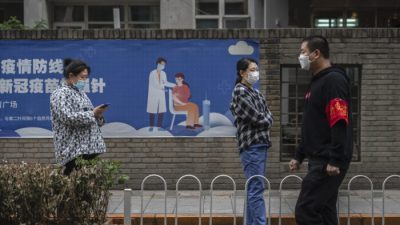 Люди стоят в очереди для сдачи анализа на нуклеиновую кислоту для выявления COVID-19 рядом с плакатом о вакцинации на импровизированном месте тестирования в Центральном деловом районе Чаоян в Пекине, Китай, 27 апреля 2022 года. (Kevin Frayer/Getty Images)