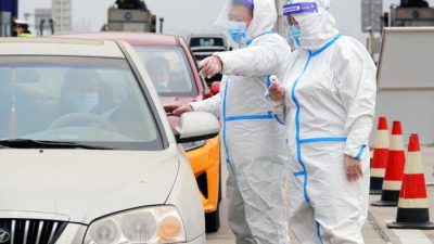 Сотрудник в средствах индивидуальной защиты направляет водителей, проверяя результаты теста на нуклеиновую кислоту и медицинские коды людей на пункте взимания дорожных сборов в Яньтае, провинция Шаньдун, Китай, 16 марта 2022 г. (STR/AFP via Getty Images)