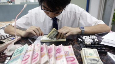 Клерк пересчитывает пачки китайских юаней и американских долларов в банке в Шанхае, Китай, 22 июля 2005. (ChinaPhotos/GettyImages)